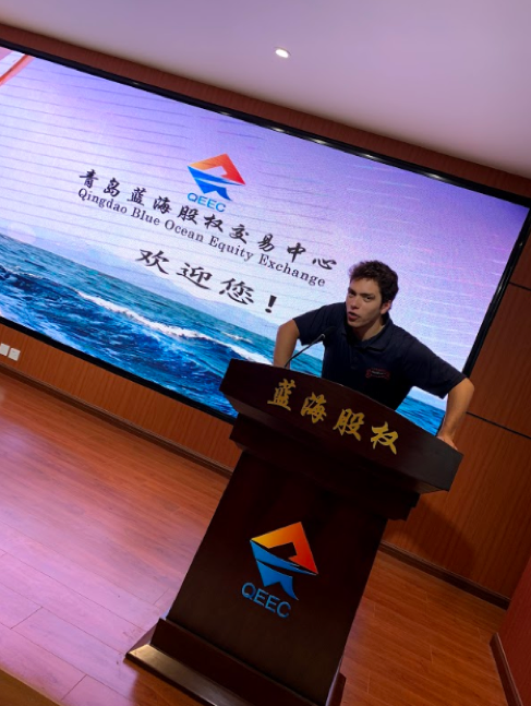 Student Rafaell Teixeira stands at a podium within the Qingdao Blue Ocean Equity Exchange Center’s building. (Qingdao, 2019)