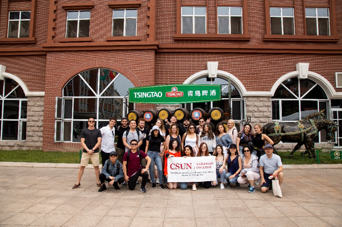 Nazarian College International Study Group students, along with Professors Tao “Eric” Hu and Kunpeng Li, stand in front of the entrance to the Tsingtao Beer Museum while holding a CSUN Nazarian College banner. (Qingdao, 2019)